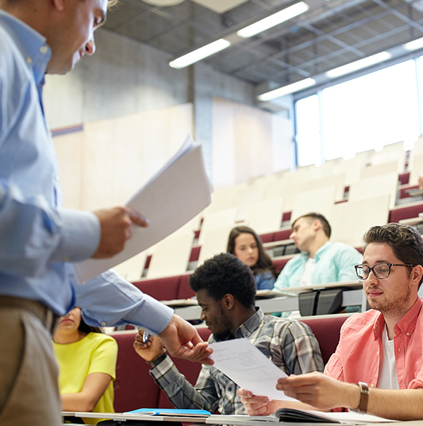 Teacher handing test paper to student in classroom with other students